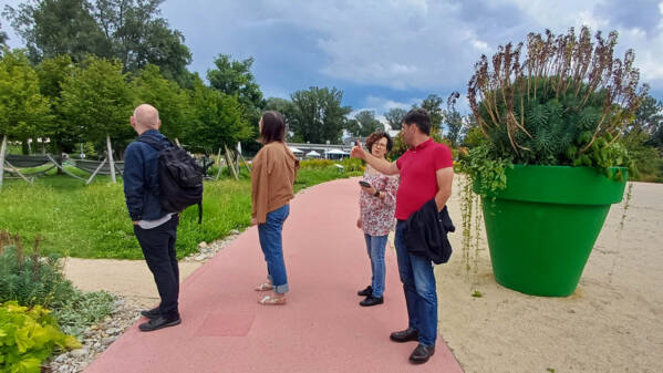 Eine Gruppe von Menschen steht auf einer Straße in einem großen Park- oder Gartengebiet. Zwei Menschen schauen sich die Umgebung an, während zwei andere eine Besprechung führen.